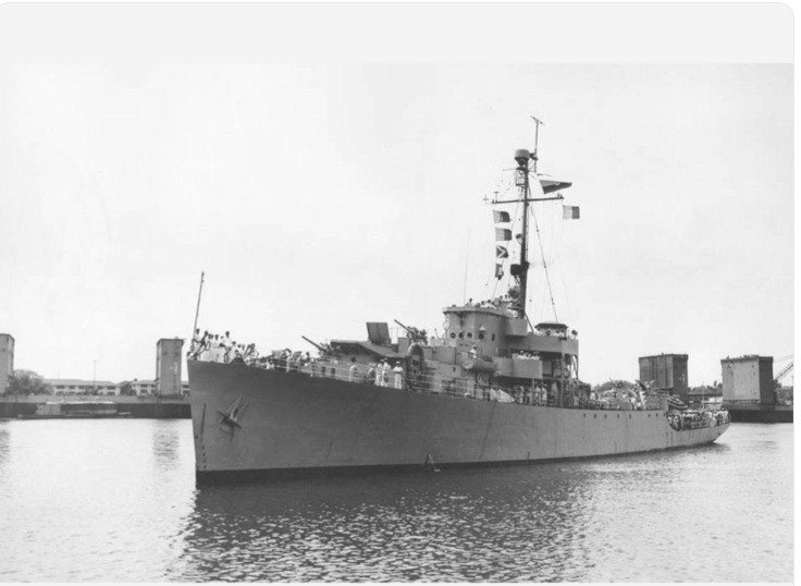 Fotografía en blanco y negro de la fragata ARC Almirante Padilla atracada en puerto, con la tripulación formada en cubierta y banderas de señales izadas en el mástil.